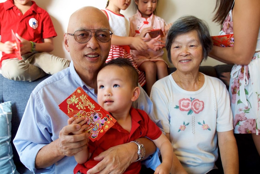 A man, woman and baby sit and hold red cards given to them on the Lunar New Year.