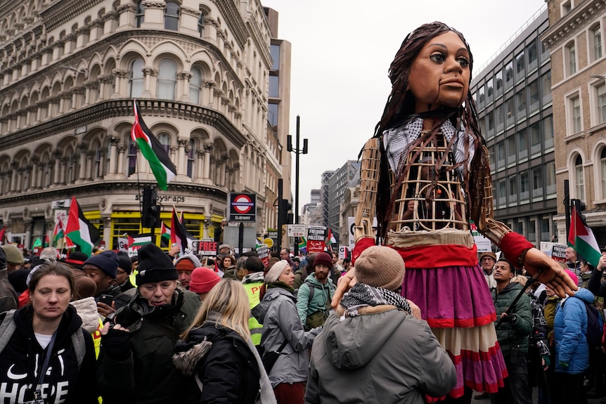 A tall puppet stands above a crowd on a street. 