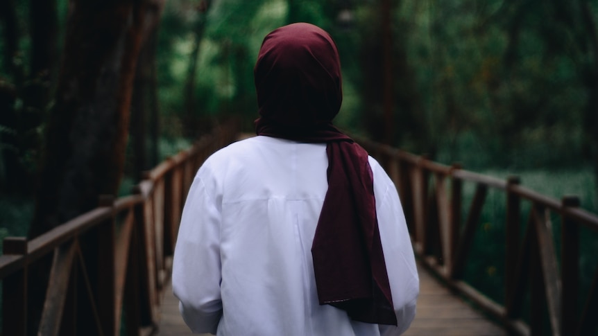 A generic image of a woman in a red hijab pictured from behind walking in forest. 
