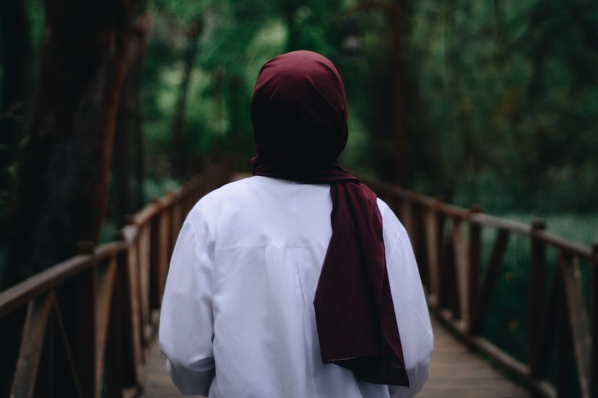 A generic image of a woman in a red hijab pictured from behind walking in forest. 