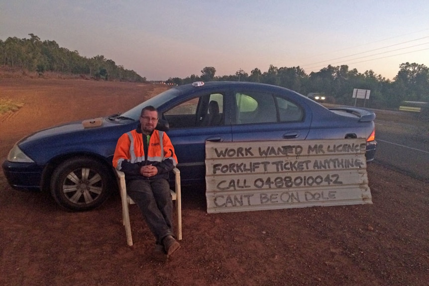 Job seeker Jeremy Moffat sits  in front of his car on the side of the Stuart Highway with a makeshift sign calling for work