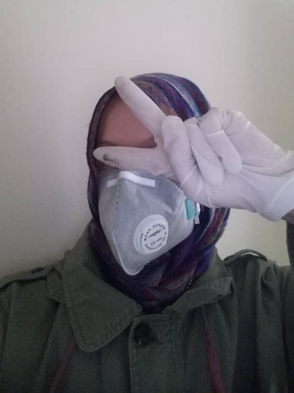 A woman pictured gesturing the peace sign wearing hijab, gloves and a face mask.