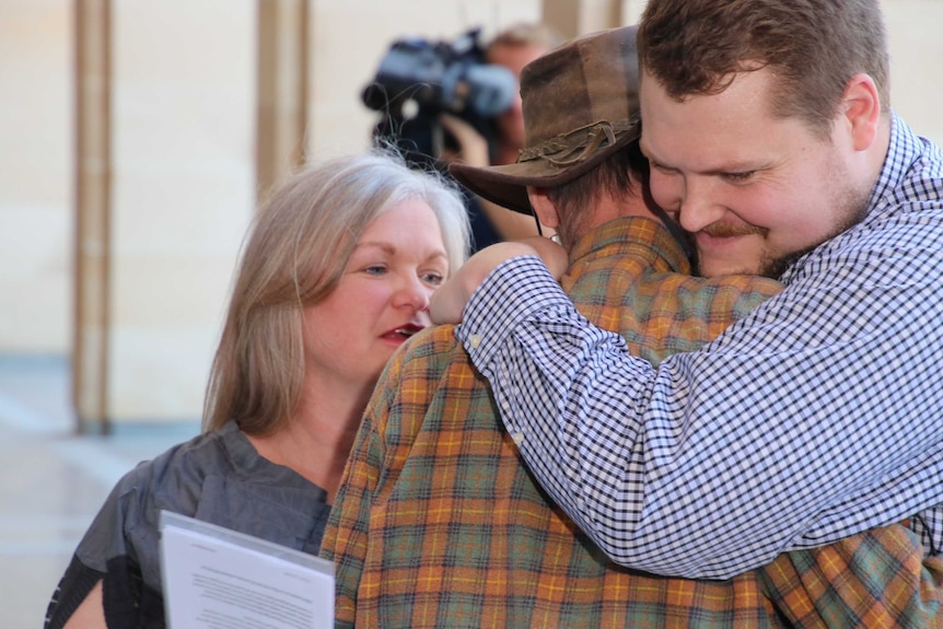 Two men and a woman embrace outside State Parliament.