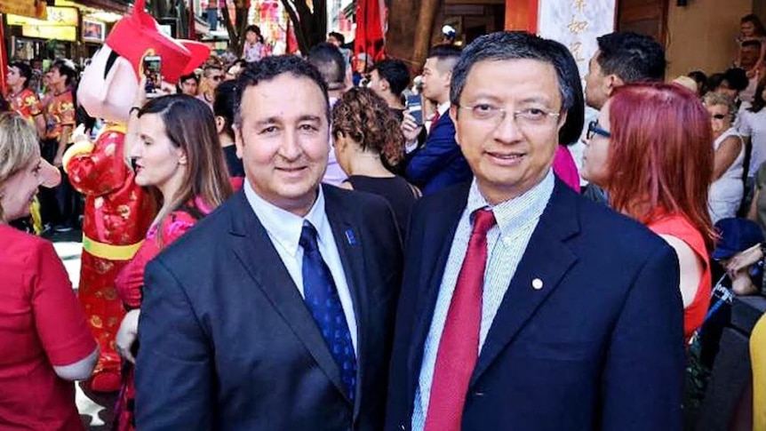 Two men wearing suits stand in busy street with many people behind them