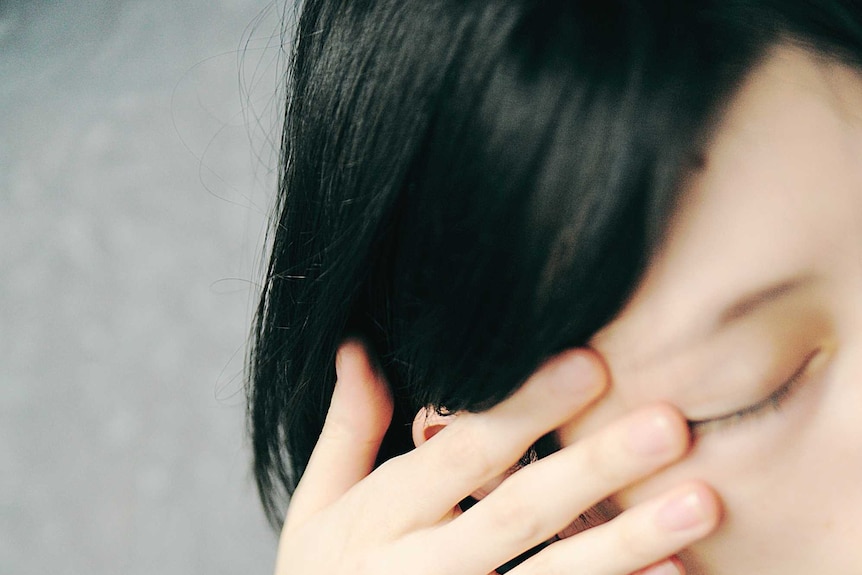 A woman puts her hands over her hair and wipes her eye.