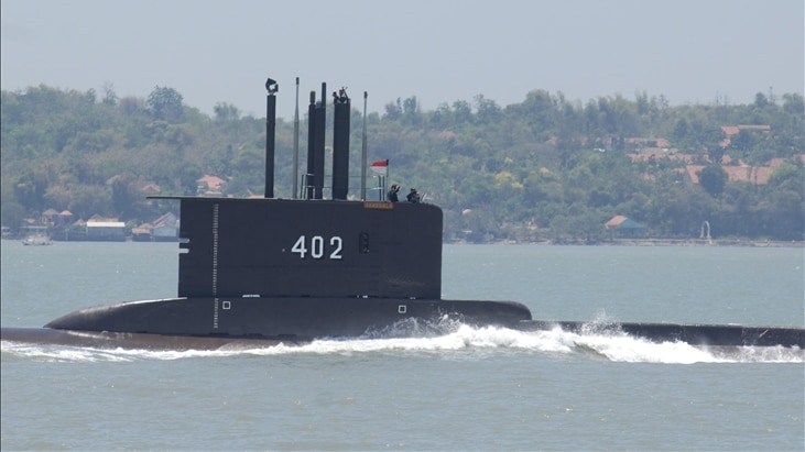 On an overcast day, a black submarine breaks the waterline with its periscope and radio antennas.