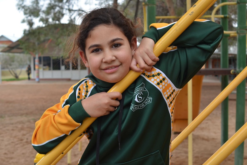 A young girl leans on a playground while in their green and gold school uniform.