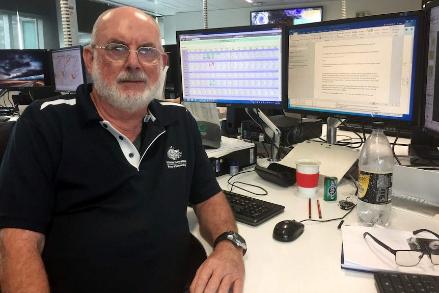 Chris Blackford sits at his desk at work with computer screens in the background.