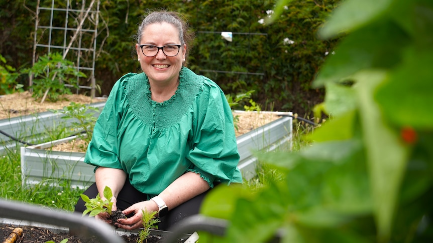 A woman in green shirt smiles while gardening.