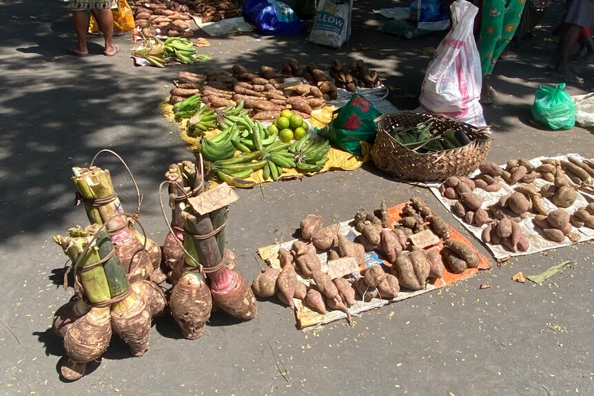 Large root vegetables laid out on sheets and in baskets along a street market road. 