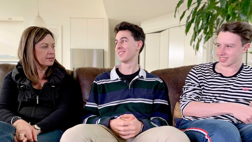 A woman sits on a couch at home with her two sons.