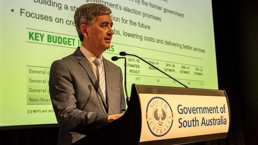 A man in a suit stands at a lecturn delivering a speech.