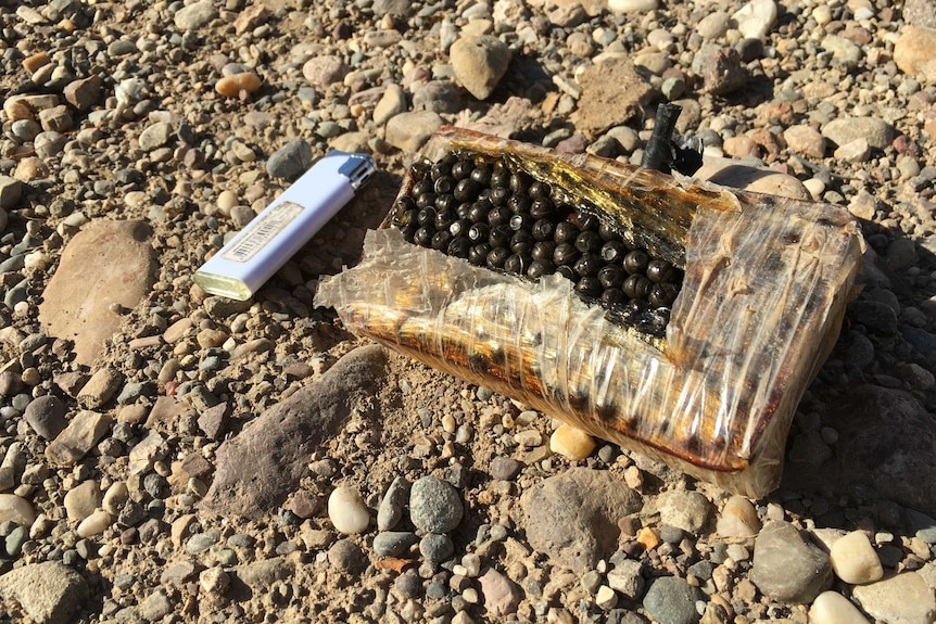 cigarette lighter next to small rectangular mine with shrapnel inside.