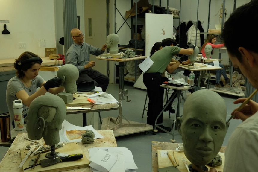 Students in an art class working on sculptures reconstructing human faces.