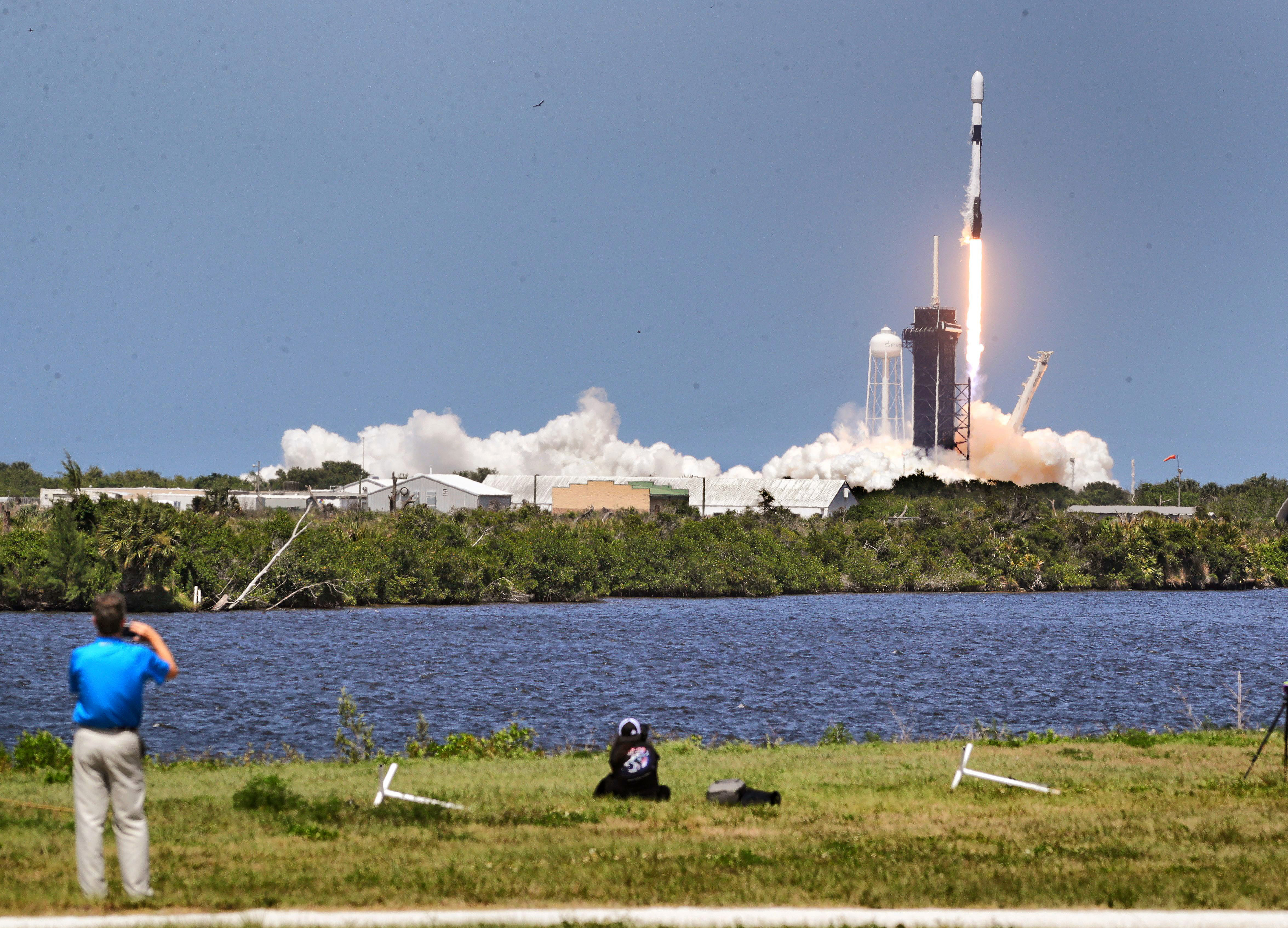A man takes a picture as a rocket launches in daylight