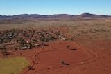 A red dirt football oval next to a grassed football oval and a small community with a mountain range in the background.