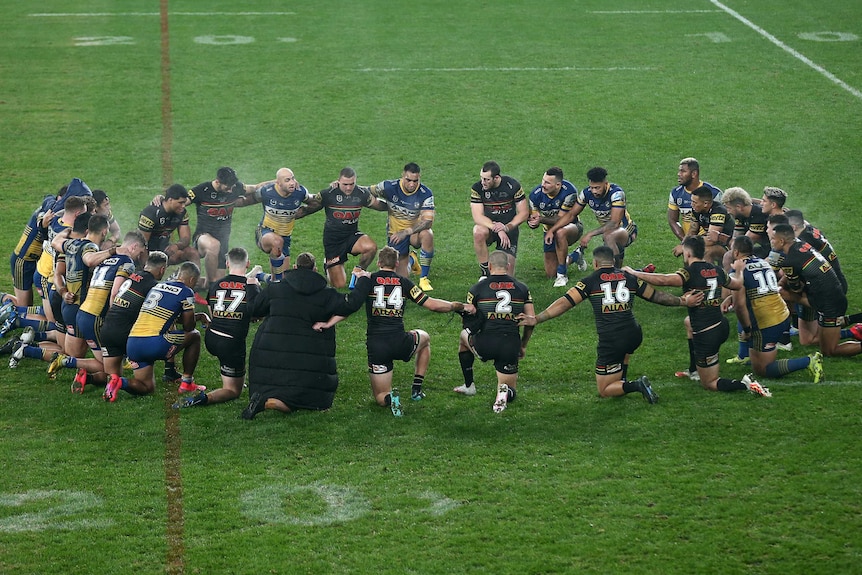 Players from both Parramatta and Penrith kneel in a circle on the field, arm in arm