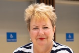 A middle-aged woman with short blonde hair sitting in an electric wheelchair