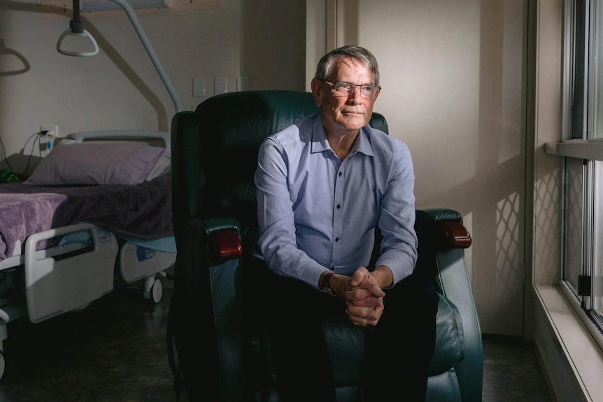 a doctor sitting in the chair next to an empty bed in a hospital ward