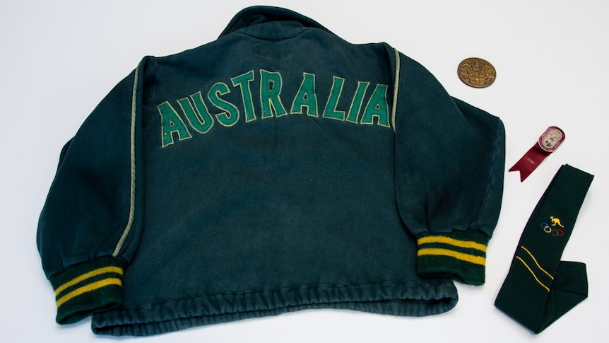 A green and gold tracksuit top with the letters 'AUSTRALIA' stitched on the back, medal, red badge with ribbon and green tie.