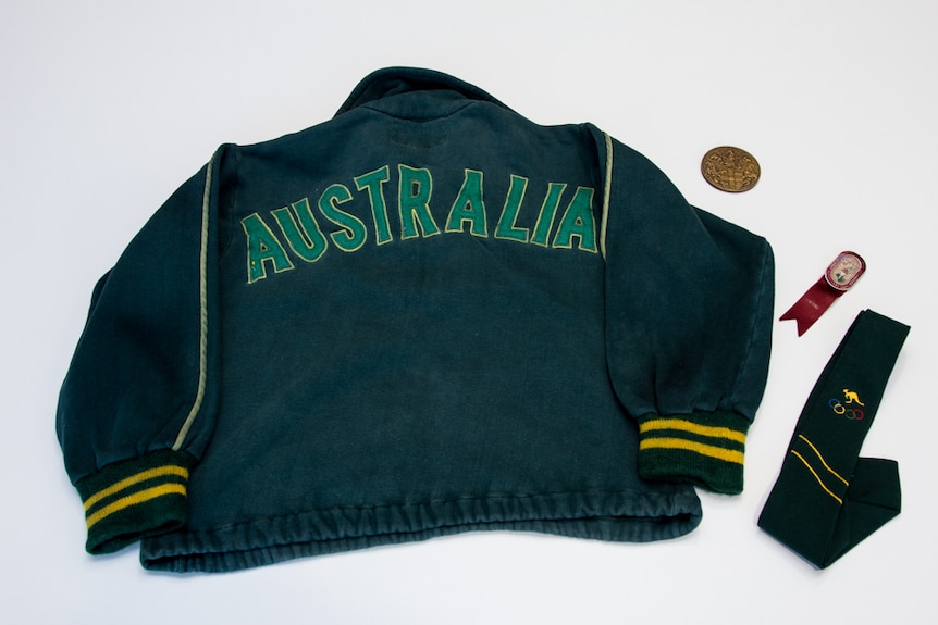 A green and gold tracksuit top with the letters 'AUSTRALIA' stitched on the back, medal, red badge with ribbon and green tie.
