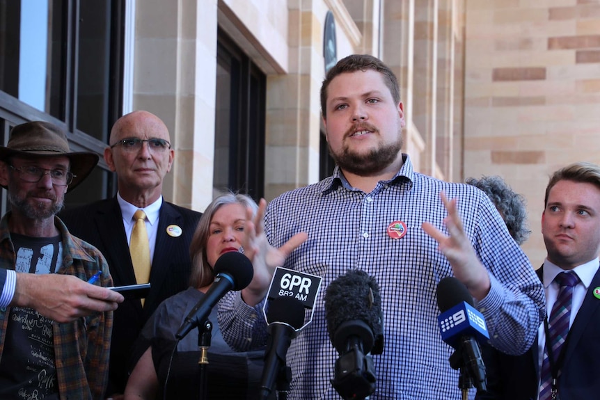 Jon Mann speaks outside WA Parliament, surrounded by a group of people including John Quigley.