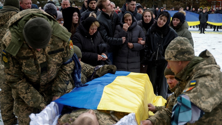 Ukrainian servicemen cover with a Ukrainian flag a coffin with the body of their brother-in-arms.