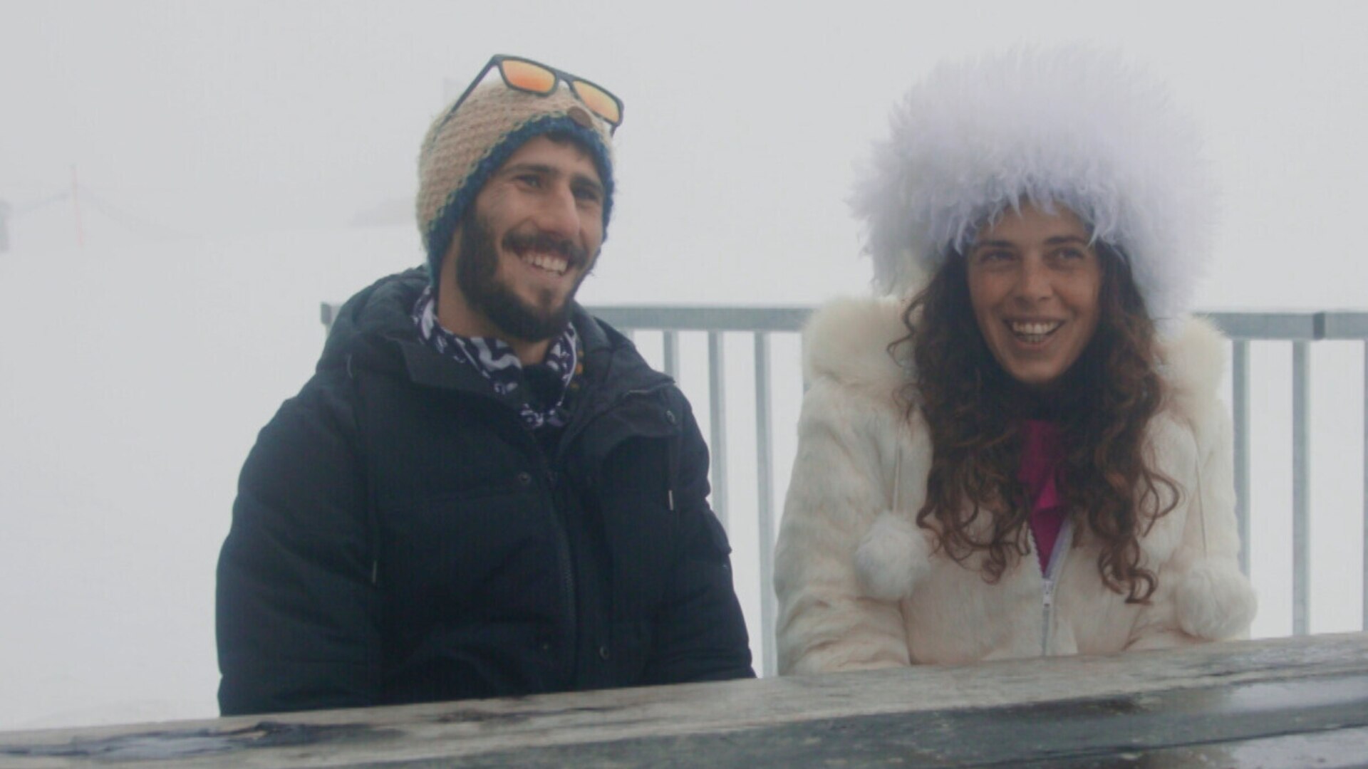 Jewish young male and female sitting outside in the snow smiling wearing ski gear 