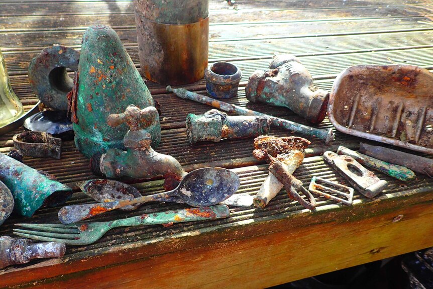 Various brass and bronze fittings, taps, fire bricks and a whistle sit on a table top near the beach.