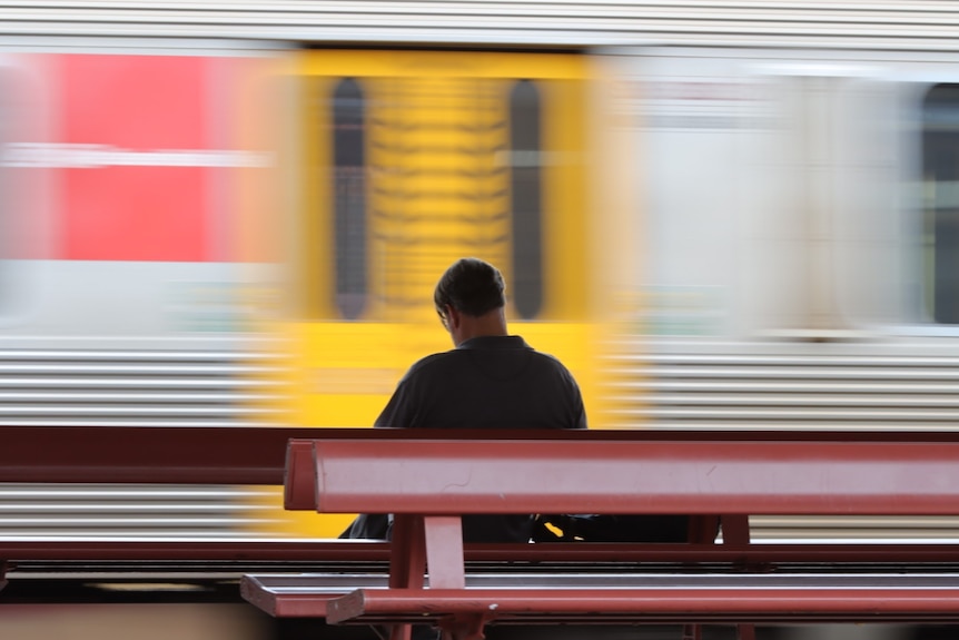 A man on a bench as the train whizzes past.