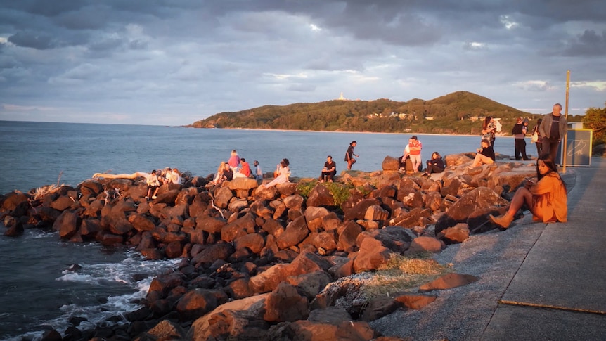 People look out over Byron Bay at sunset.