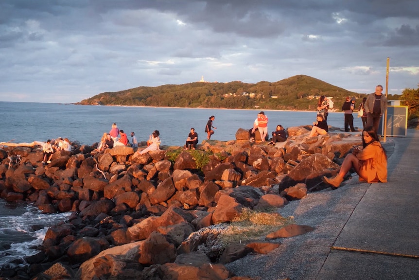 People look out over Byron Bay at sunset.