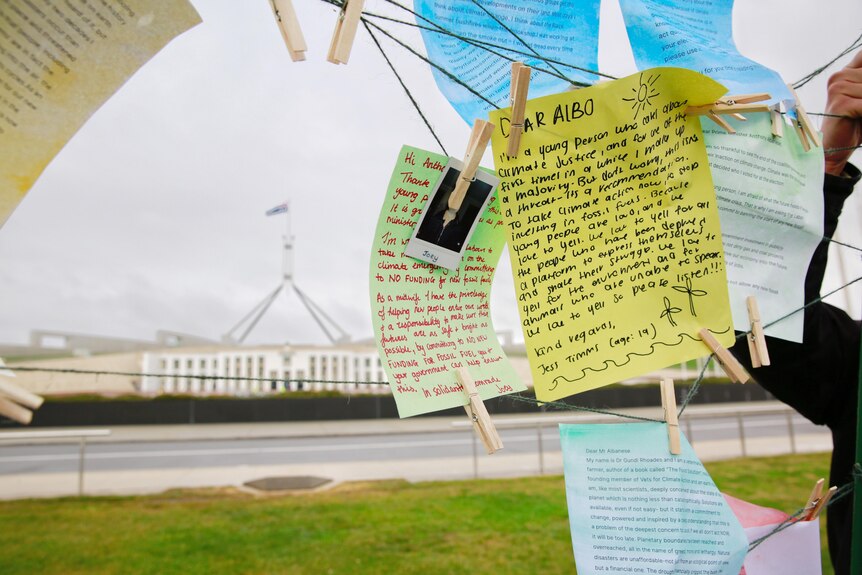 Several handwritten notes hand pegged onto a wire, with Parliament House visible in the background.