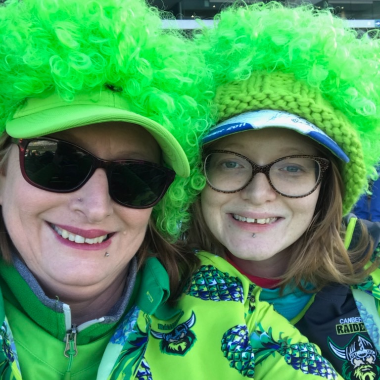 Two women wearing bright green clothes and wigs smile at the camera.