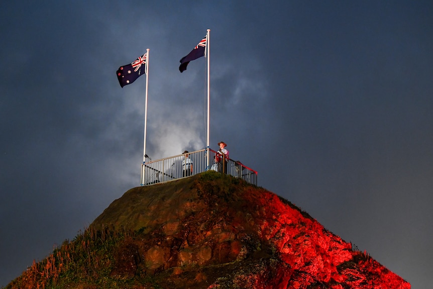 flags fly on poles sitting atop a large rock with a viewing platform where defence personnel are standing