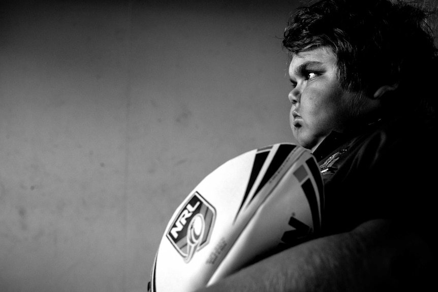 A black and white photograph of a boy holding a football