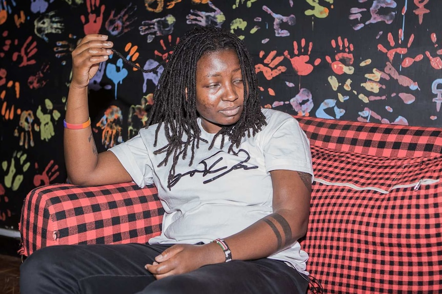Gay rights activist Mercy Njueh sits on a couch in front of a brightly coloured wall