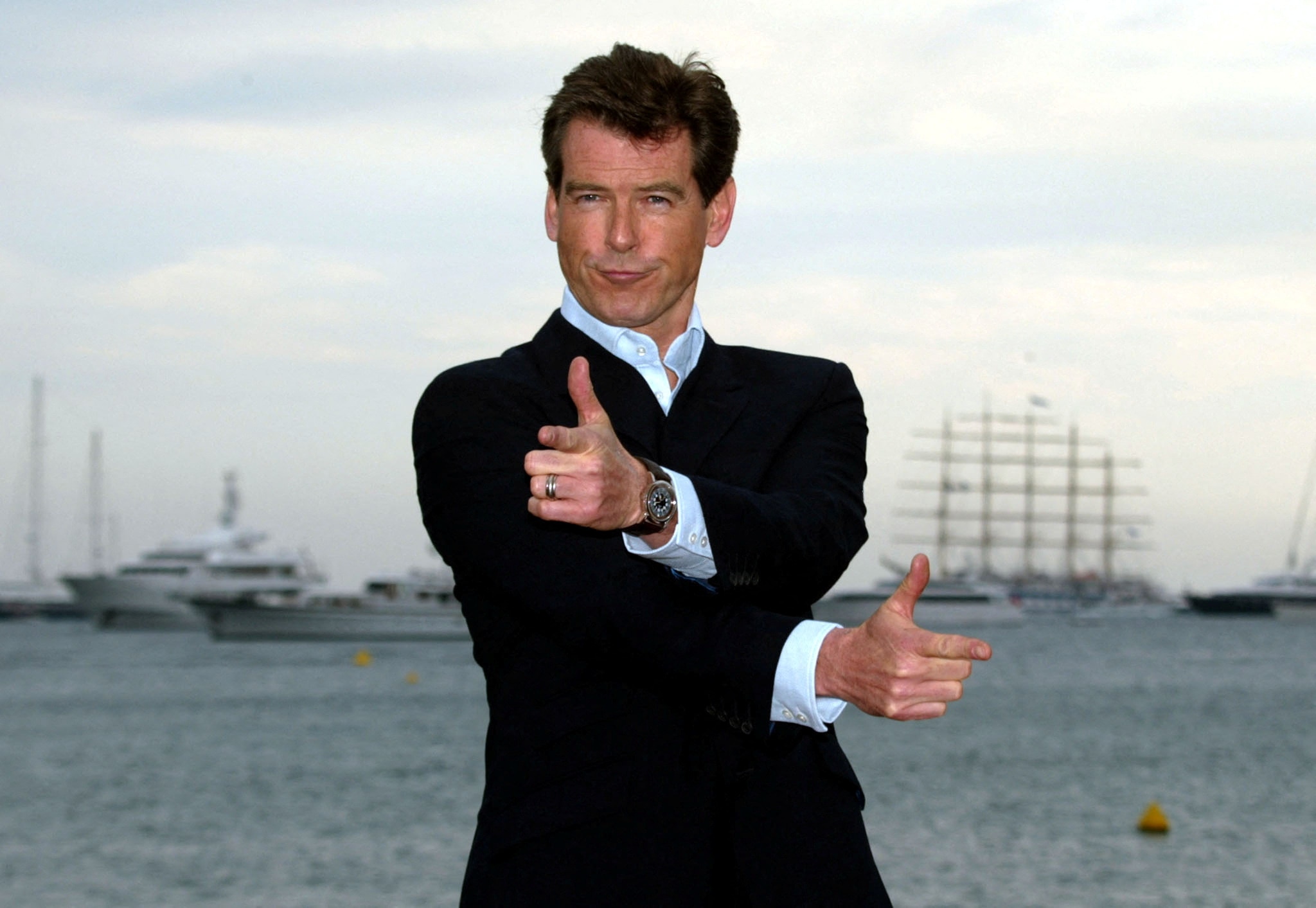 A man in a suit posing doing finger guns. 