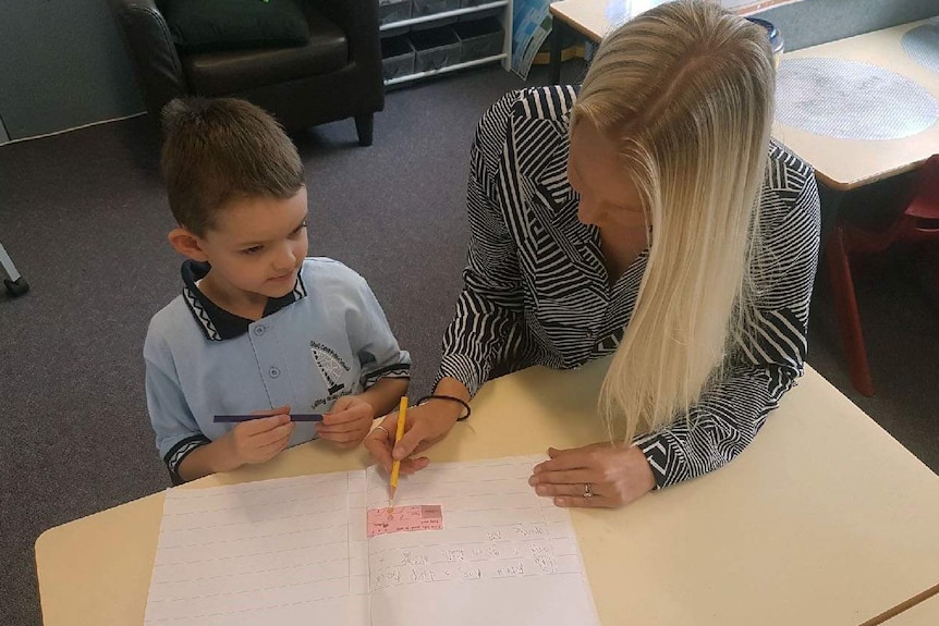 A teacher sits with a pupil and his test paper