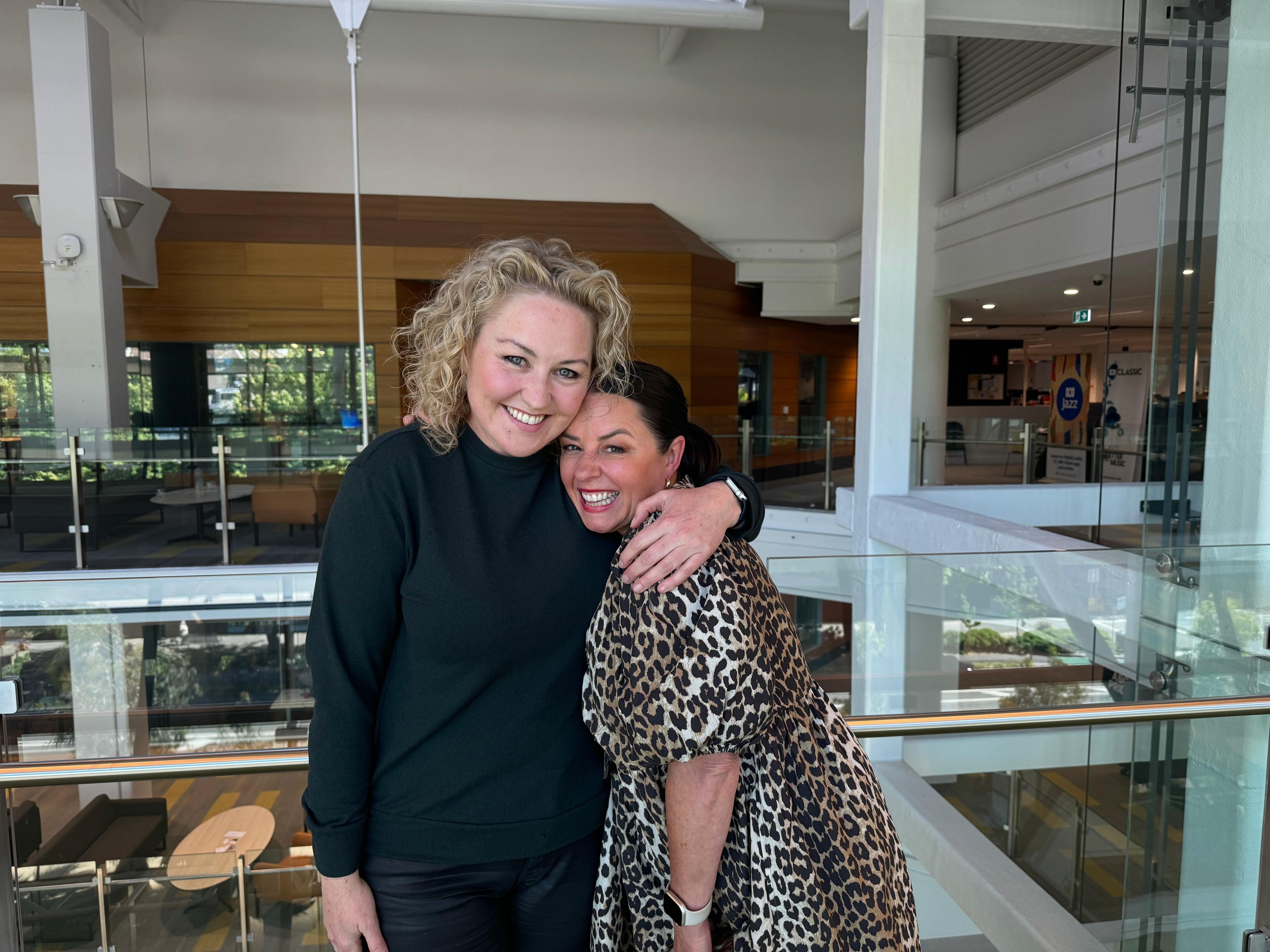 Zan and Myf with their arms around one another, Zan wears black and Myf wears leopard print