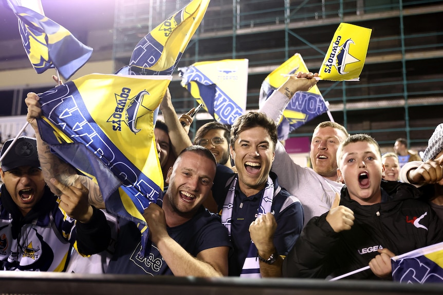 A group of North Queensland Cowboys fans grin and wave their flags in the crowd after a win.