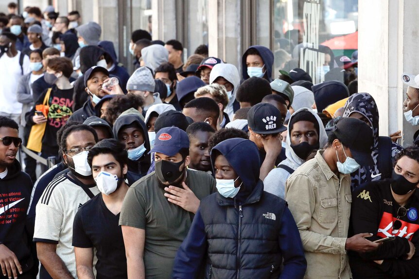 People, some wearing masks, others not, queue outside London stores.