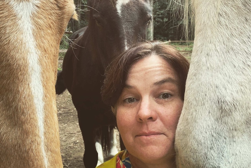 Woman with brown hair and yellow top is surrounded by three horse