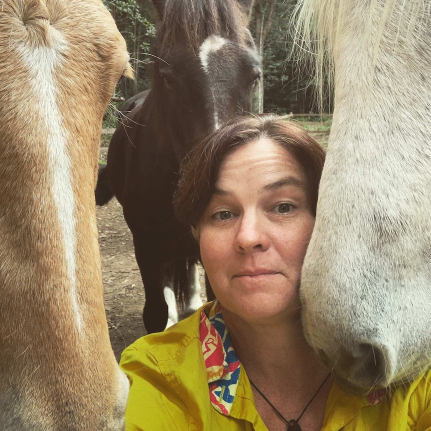 Woman with brown hair and yellow top is surrounded by three horse