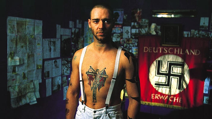 A bare-chested man with tattoos stands in front of a Nazi flag