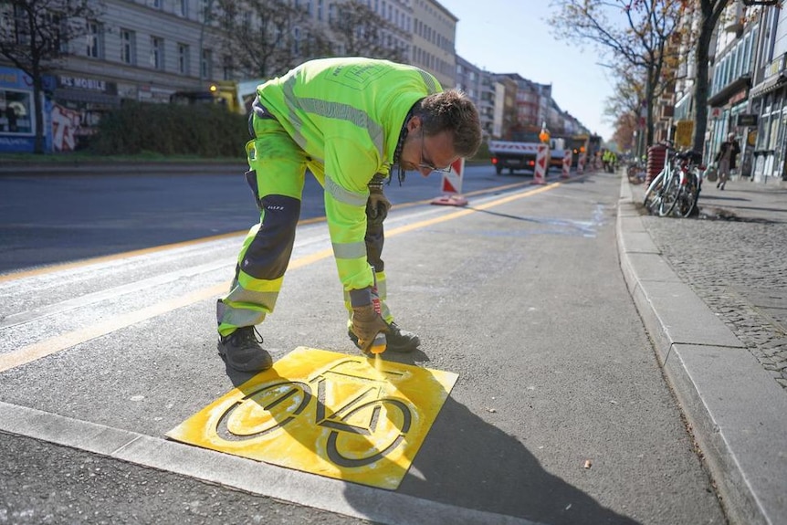 A man spray paints a bicycle picture onto the road.