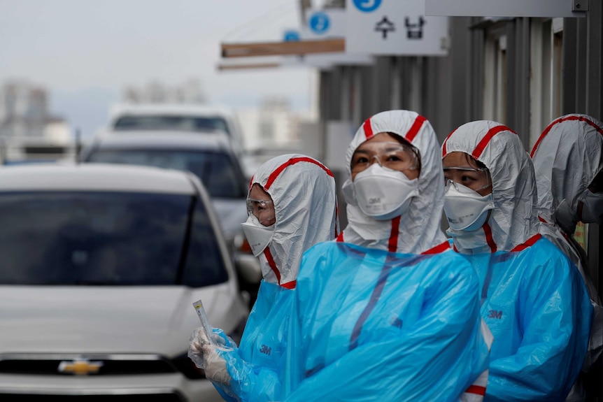 Workers in testing suits looking at cars