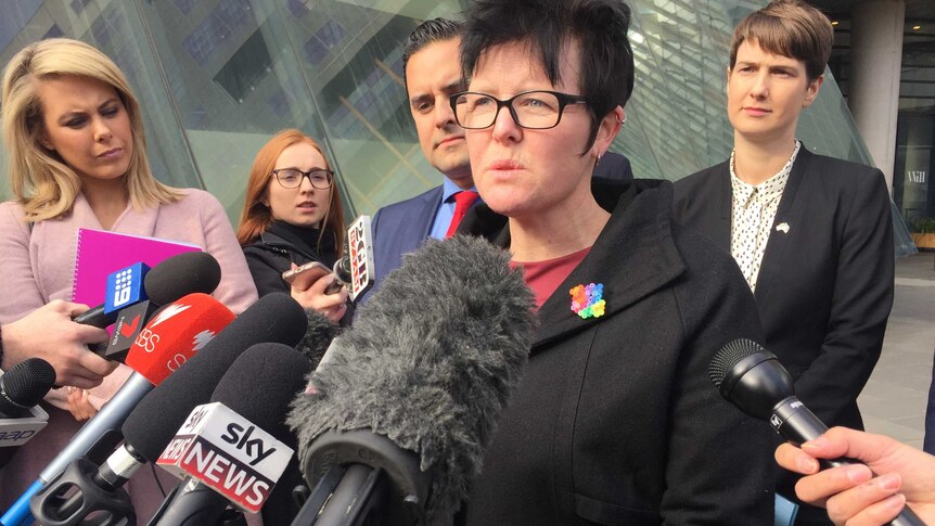A woman with a rainbow coloured brooch speaks to the media.