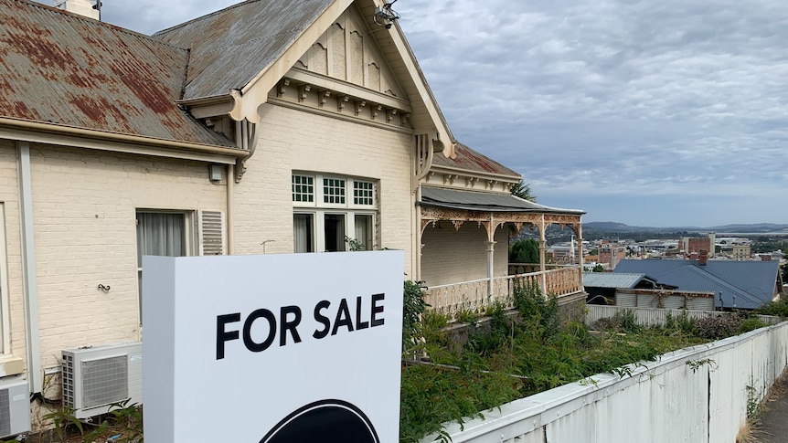 A for sale sign in front of a rundown house