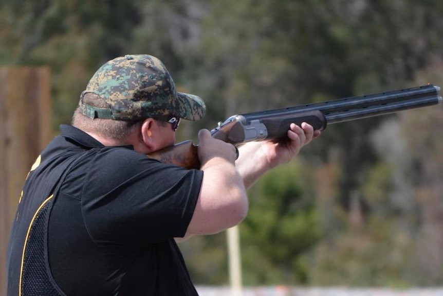 Man standing side on holding a gun preparing to shoot